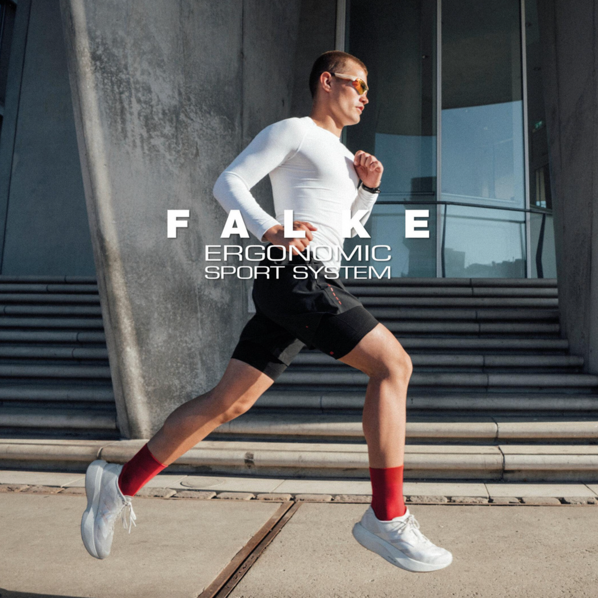 A man running outdoors in front of a modern concrete building, wearing a white long-sleeve athletic top, black shorts, white running shoes, and red socks. Large overlaid text reads 'FALKE ERGONOMIC SPORT SYSTEM'.