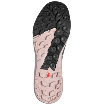 The outsole of a trail running shoe, showing a black treaded section on the heel and a light pinkish-beige section on the forefoot with a small red triangular logo.