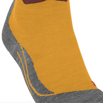 A close-up of a low-cut sock with a mustard yellow main body, gray heel and toe, and a wavy pattern of brown, rust, and light blue near the cuff, shown on a white background.