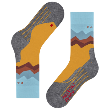 A pair of crew socks shown flat on a white background, featuring a mountain landscape design with a mustard yellow field, brown and red peaks, light blue sky layers, and heather gray toe/heel areas with yellow line details.